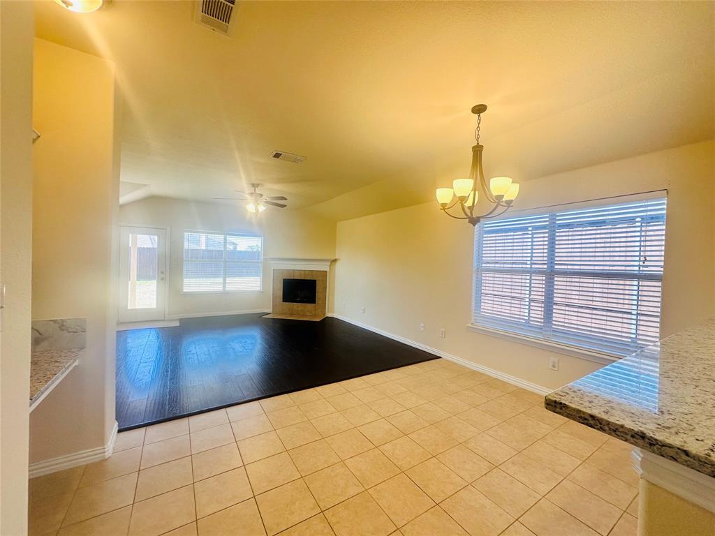 Unfurnished living room with a tiled fireplace, ceiling fan with notable chandelier, lofted ceiling, and light tile patterned flooring