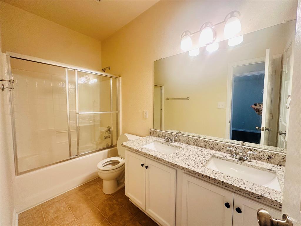 Full bathroom with tile patterned flooring, vanity, toilet, and combined bath / shower with glass door