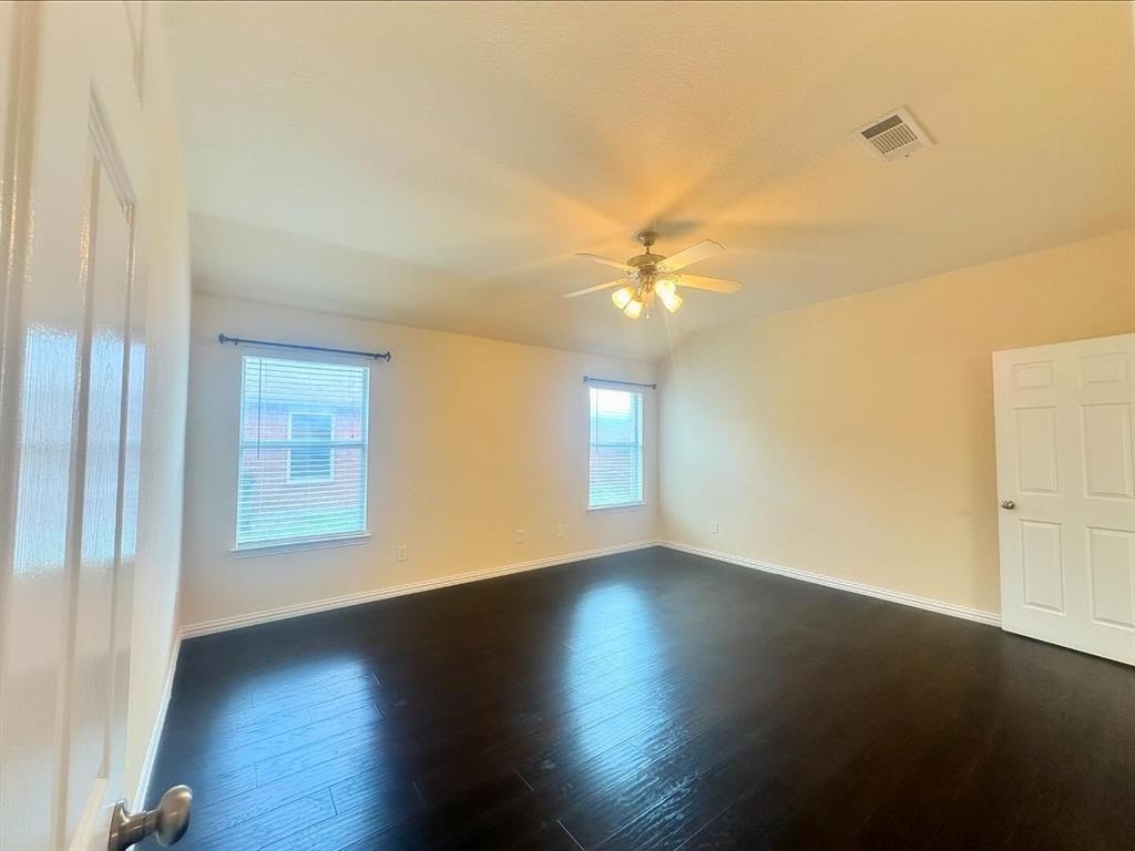 Empty room with a healthy amount of sunlight, dark hardwood / wood-style floors, and ceiling fan