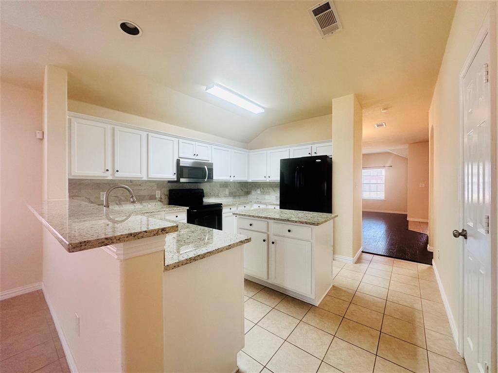 Kitchen with decorative backsplash, kitchen peninsula, white cabinets, and black appliances