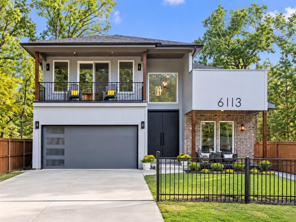 Modern two-story exterior featuring a brick facade, wood-finish support columns, a covered balcony with metal railing, and a multi-panel garage door