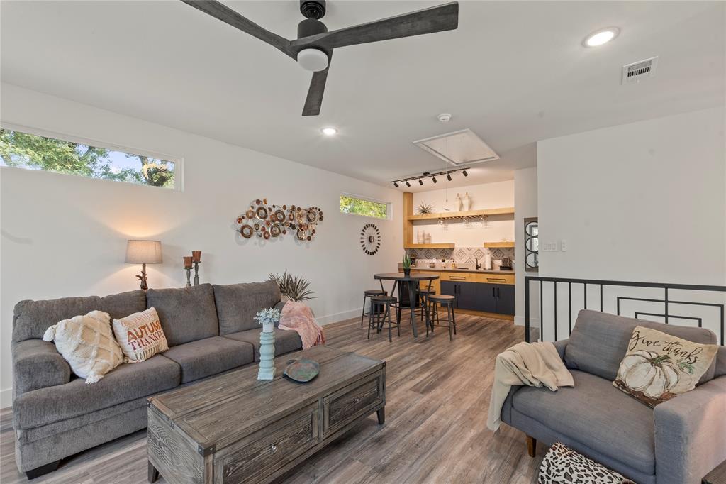 Wood-finish flooring, matte black three-blade ceiling fan, transom windows, built-in wet bar with natural wood shelving, and patterned tile backsplash