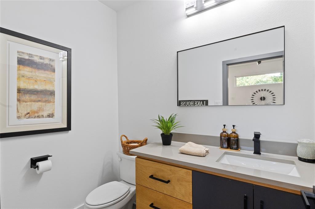 Vanity featuring dual-tone cabinetry, stone-composite countertop with integrated sink, matte black faucet, and rectangular wall-mounted mirror