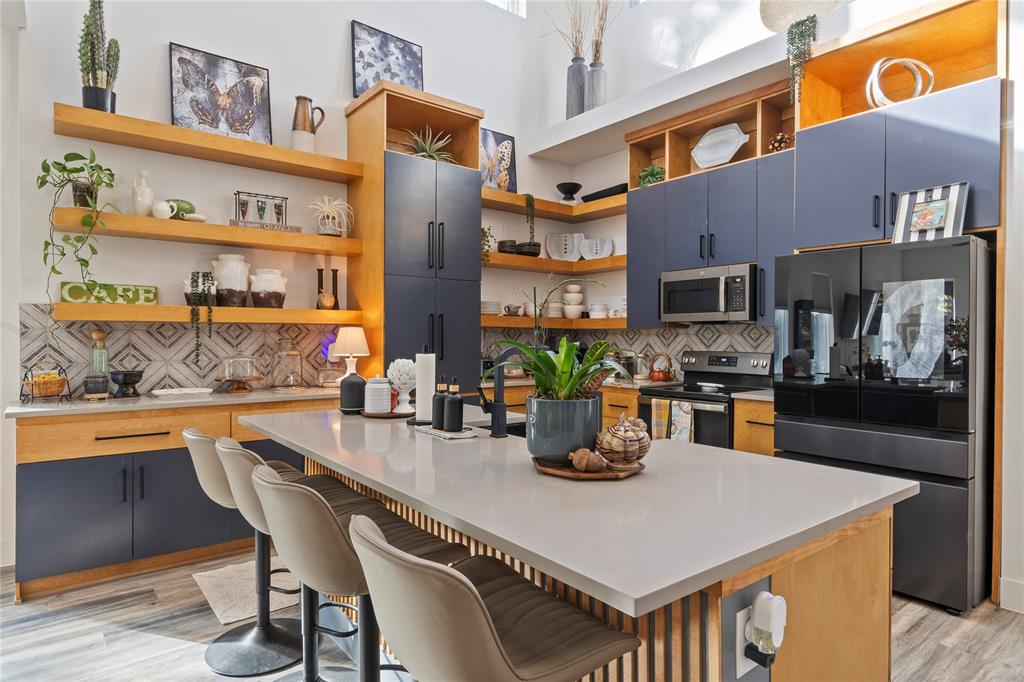 Kitchen featuring dual-toned flat-panel cabinetry, open wood shelving, a quartz-topped island with vertical slat detailing, and a geometric patterned tile backsplash
