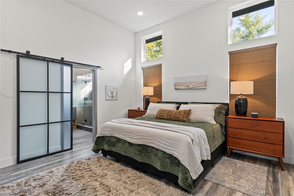 High ceilings featuring stacked windows, wood-finish flooring, and a sliding barn door with frosted glass panels and black metal hardware High ceilings featuring stacked windows, wood-finish flooring, and a sliding barn door with frosted glass panels and black metal hardware