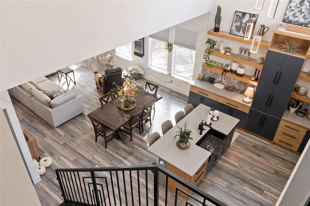 Open-concept interior featuring two-story ceilings, wood-finish flooring, and a kitchen island with a rectangular basin sink and matte black hardware