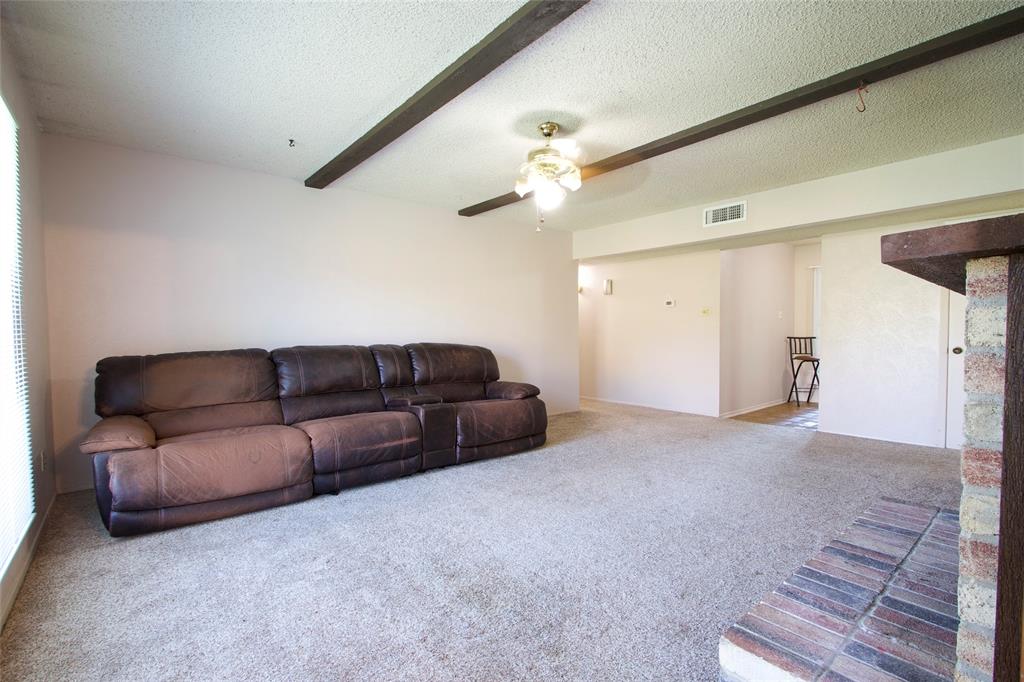 Living area featuring exposed wooden ceiling beams, a ceiling fan with integrated lighting, and a brick fireplace hearth