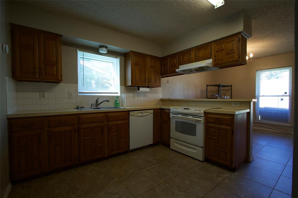 Kitchen featuring wood cabinetry, tile flooring, white tile backsplash, integrated range hood, and double-basin sink