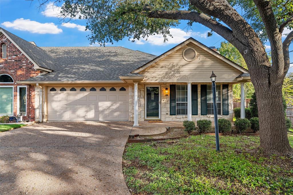 Exterior facade featuring mixed stone and horizontal siding, arched window detail, covered front porch with columns, and a textured concrete driveway