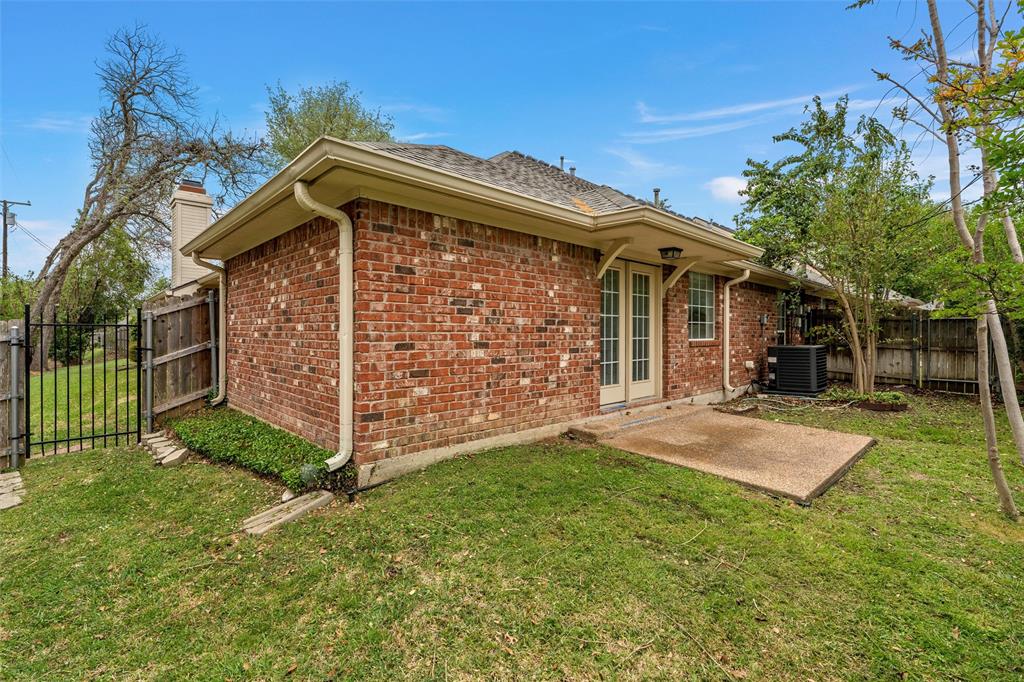 Rear exterior featuring red brick masonry, a concrete patio, French doors, and metal perimeter fencing