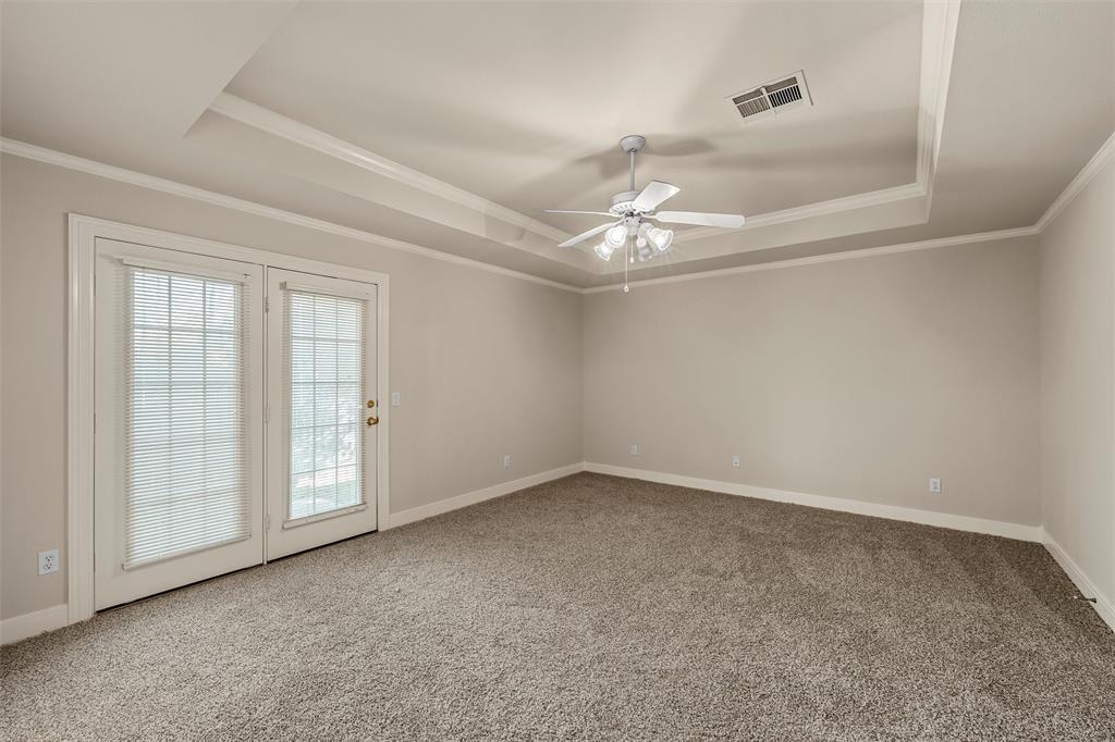 Tray ceiling with crown molding, neutral carpeting, and glass-paned double doors leading to the exterior