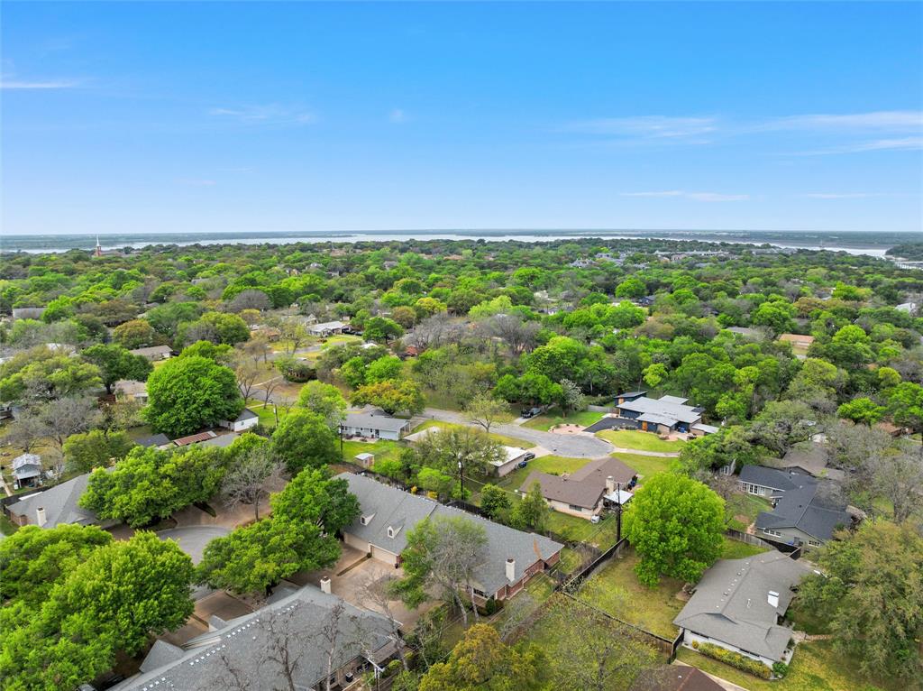 Aerial perspective of a suburban neighborhood featuring mature trees, paved roadways, and residential structures with shingled roofing