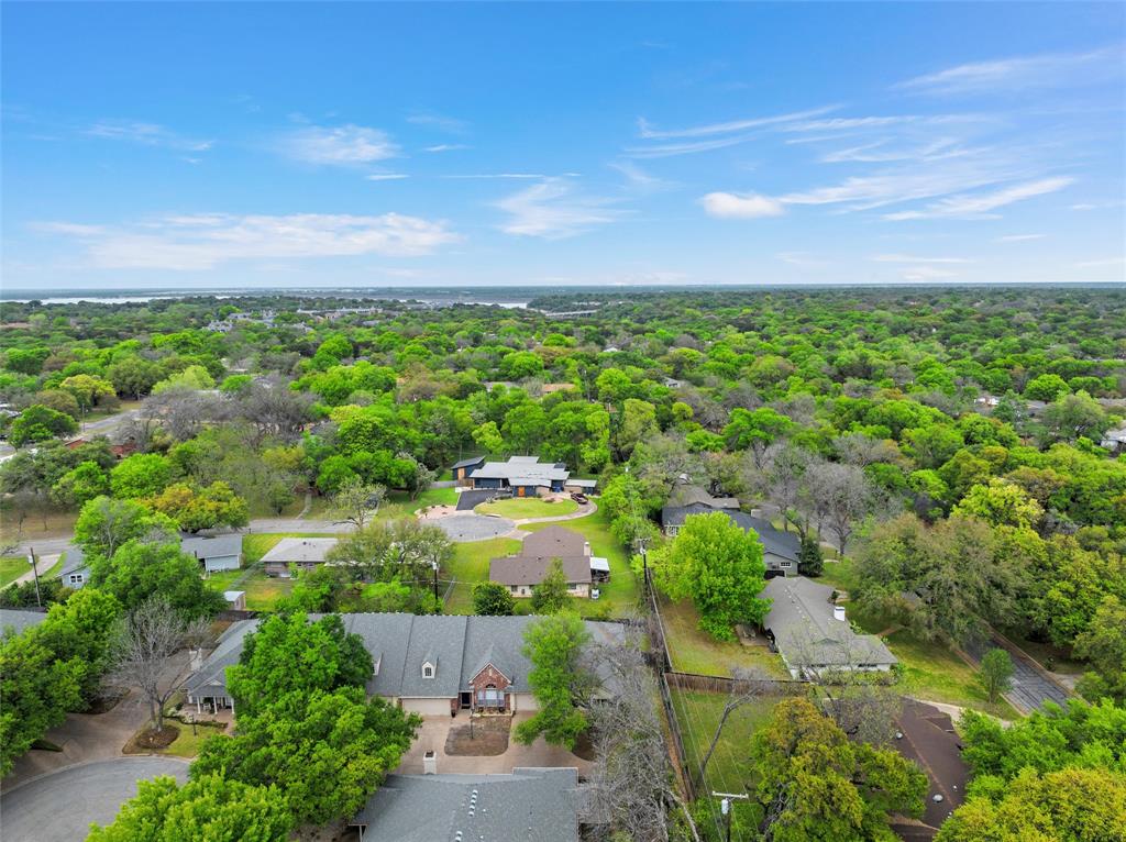 Aerial perspective of a sprawling residential area featuring extensive tree coverage, winding suburban streets, and multiple homes with pitched rooflines