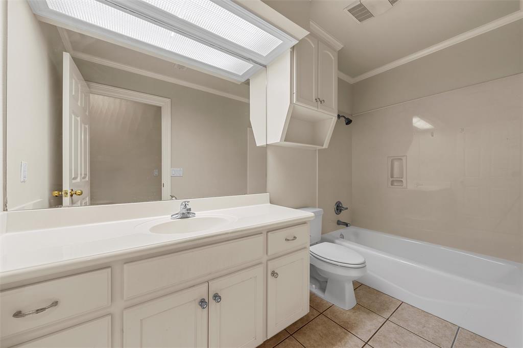 Bathroom featuring a white vanity with integrated basin, solid surface countertop, large wall-mounted mirror, overhead cabinetry, and a shower-tub combination with tile-surround