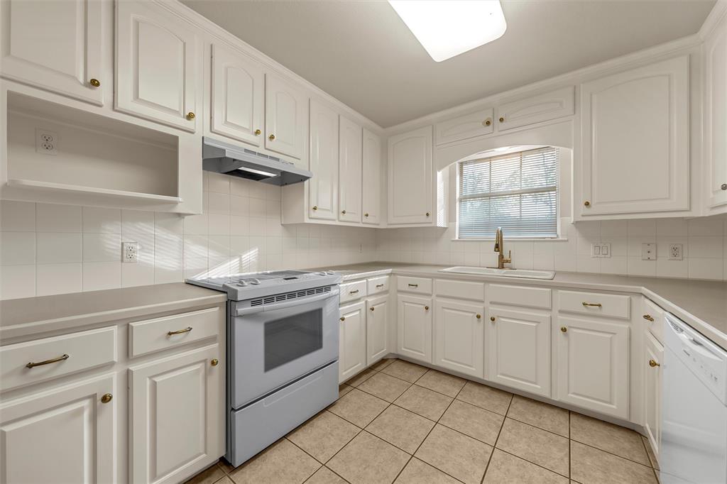 Kitchen featuring white shaker-style cabinetry, solid surface countertops, ceramic tile backsplash, tiled flooring, and a built-in range hood Kitchen featuring white shaker-style cabinetry, solid surface countertops, ceramic tile backsplash, tiled flooring, and a built-in range hood