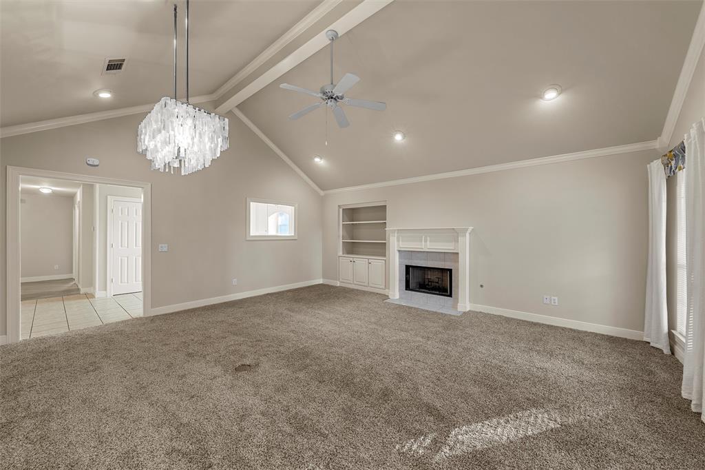 Vaulted ceiling featuring recessed lighting, a central crystal chandelier, and a ceiling fan, complemented by a stone-surround fireplace and custom built-in cabinetry Vaulted ceiling featuring recessed lighting, a central crystal chandelier, and a ceiling fan, complemented by a stone-surround fireplace and custom built-in cabinetry