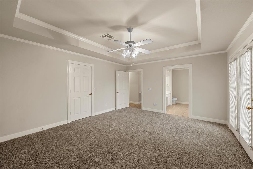 Tray ceiling, central ceiling fan with multi-light fixture, carpeted flooring, and double glass-paned doors