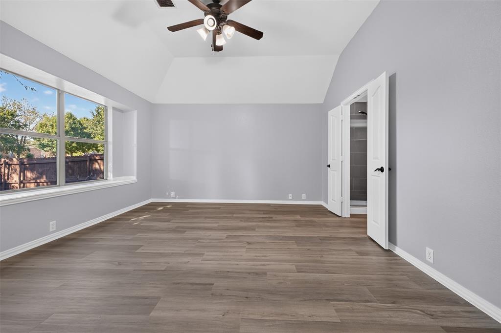 Vaulted ceiling with a central multi-light fan, wood-finish flooring, large window, and double-door entry
