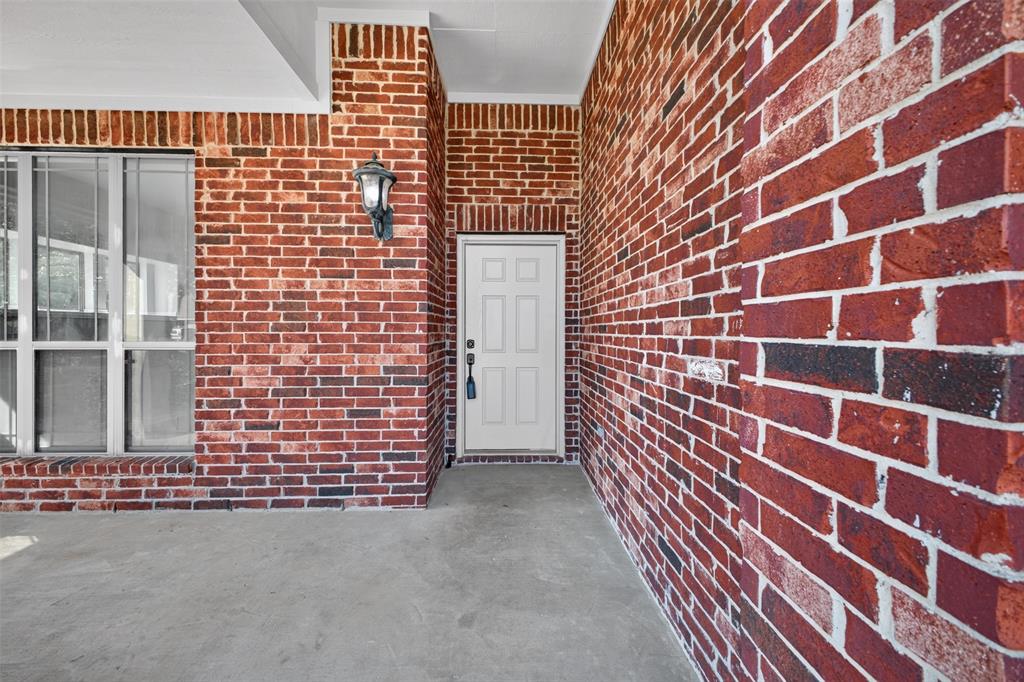Covered entrance featuring red brick exterior, multi-pane window, and wall-mounted lantern-style lighting fixture