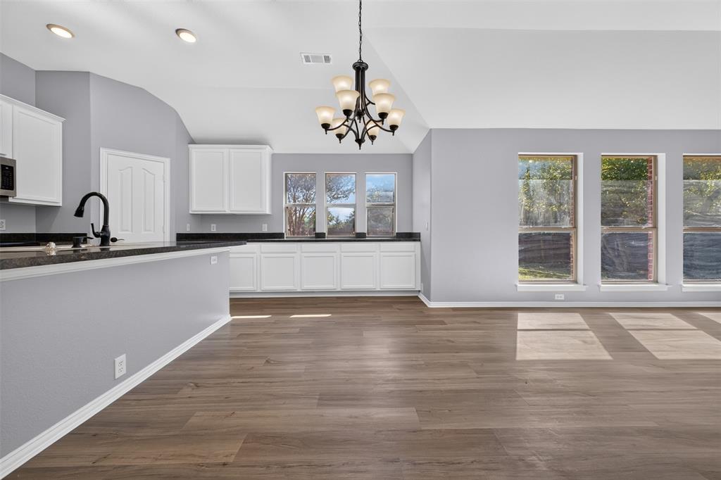 Vaulted ceilings, wood-finish flooring, white cabinetry, dark countertops, and a multi-arm chandelier