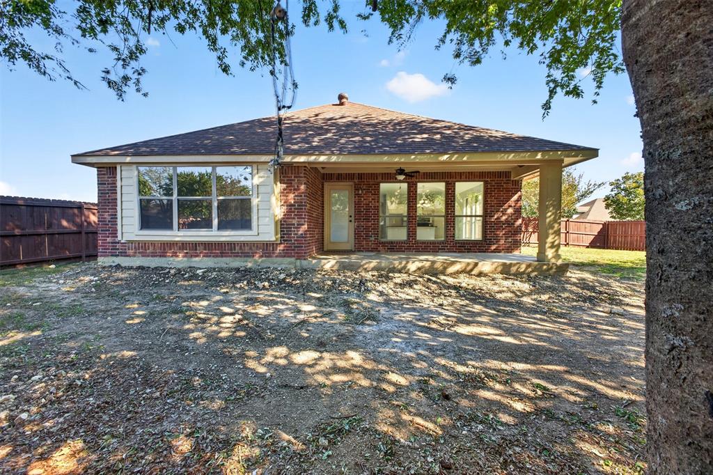 Brick exterior featuring a covered rear patio, hipped roofline, and wood-style fencing