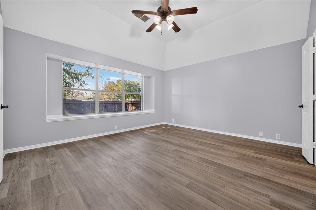 Vaulted ceiling featuring a central multi-blade ceiling fan with integrated lighting, wood-finish flooring, and expansive windows