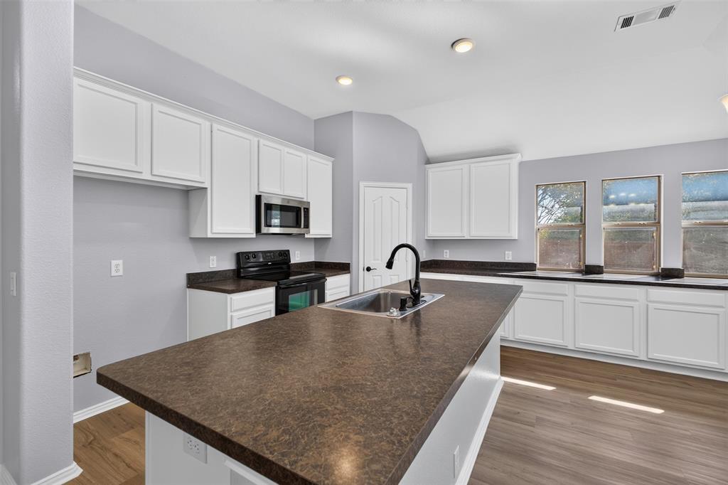 Kitchen featuring white shaker-style cabinetry, a dark-toned laminate countertop, center island with a stainless steel sink and matte black faucet, and wood-finish flooring