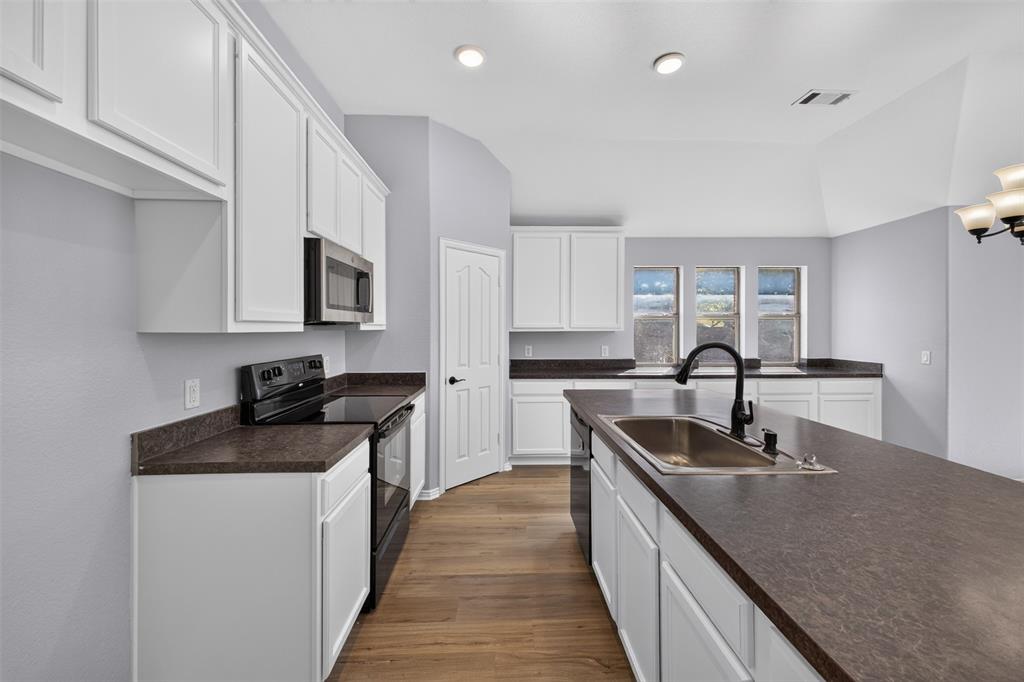 Kitchen featuring white cabinetry, dark solid-surface countertops, wood-finish flooring, a stainless steel undermount sink with a matte black faucet, and recessed lighting