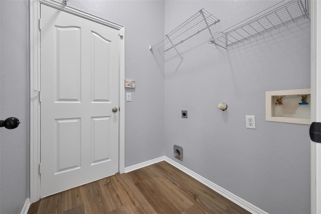 Utility room featuring wood-finish flooring, a four-panel door with a round knob, and wall-mounted wire shelving
