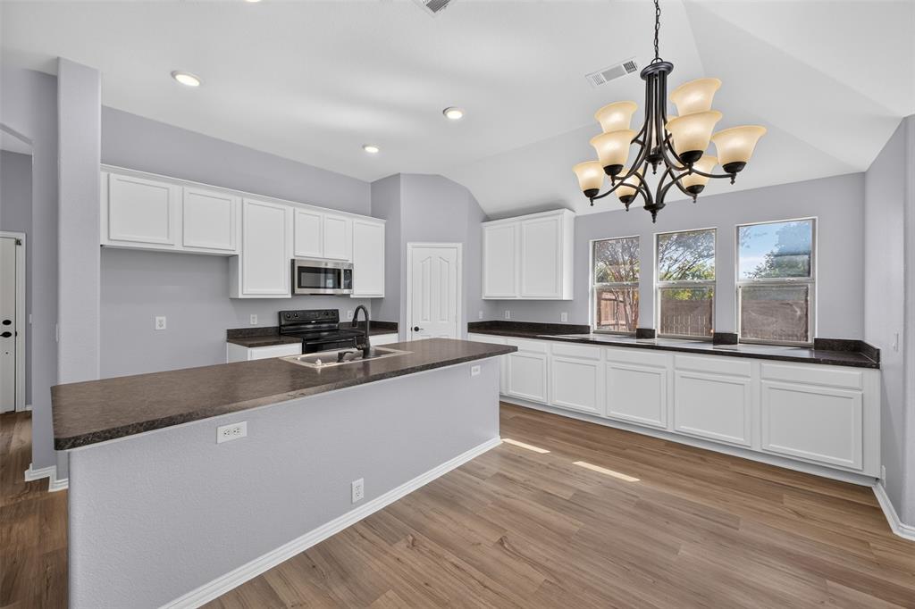 Kitchen featuring white shaker-style cabinetry, dark stone-finish countertops, wood-finish flooring, vaulted ceilings with a multi-arm chandelier, and recessed lighting