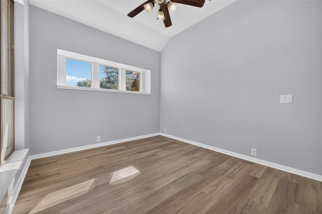 Vaulted ceiling, wood-finish flooring, horizontal window bank, and multi-blade ceiling fan