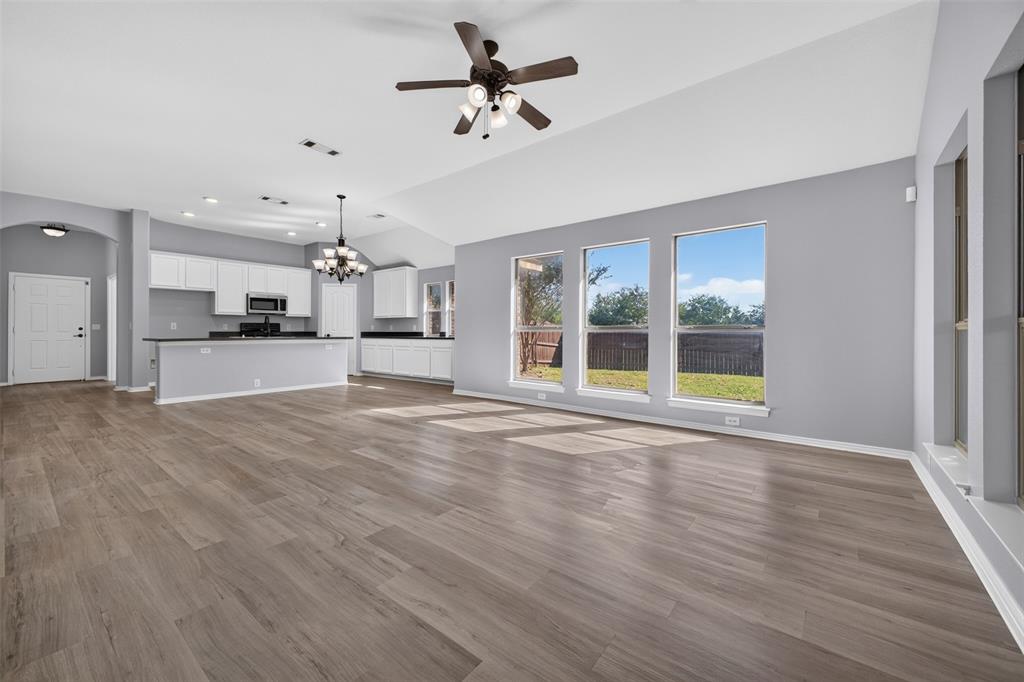 Open-concept interior featuring vaulted ceilings, wood-finish flooring, a kitchen with white cabinetry, dark countertops, and large windows