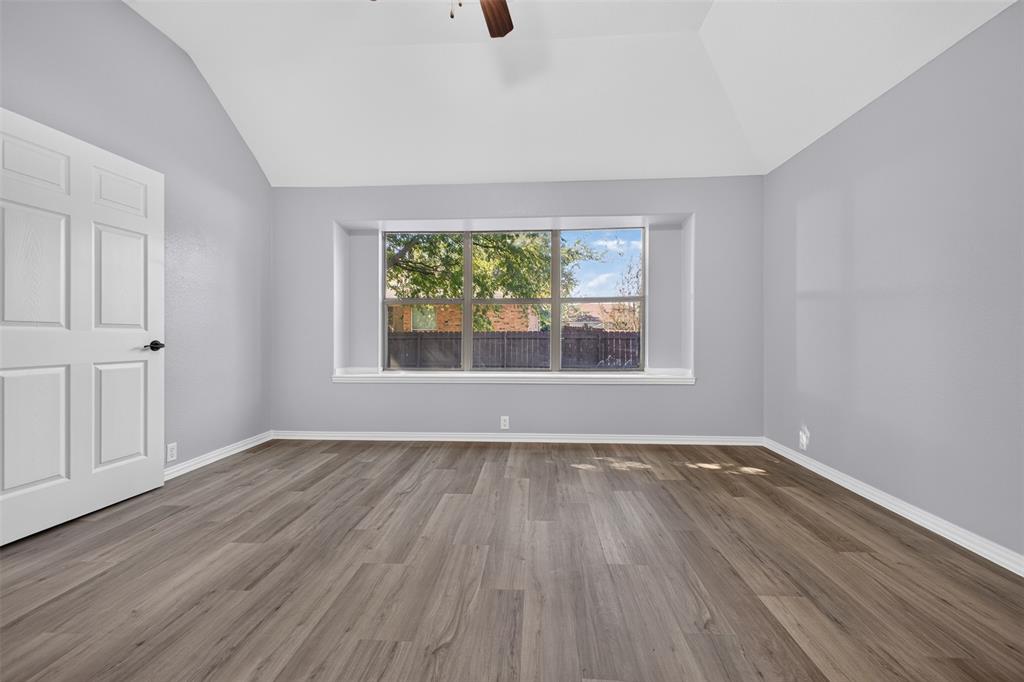 Room featuring vaulted ceilings, wood-finish flooring, and a large bay window with a sill