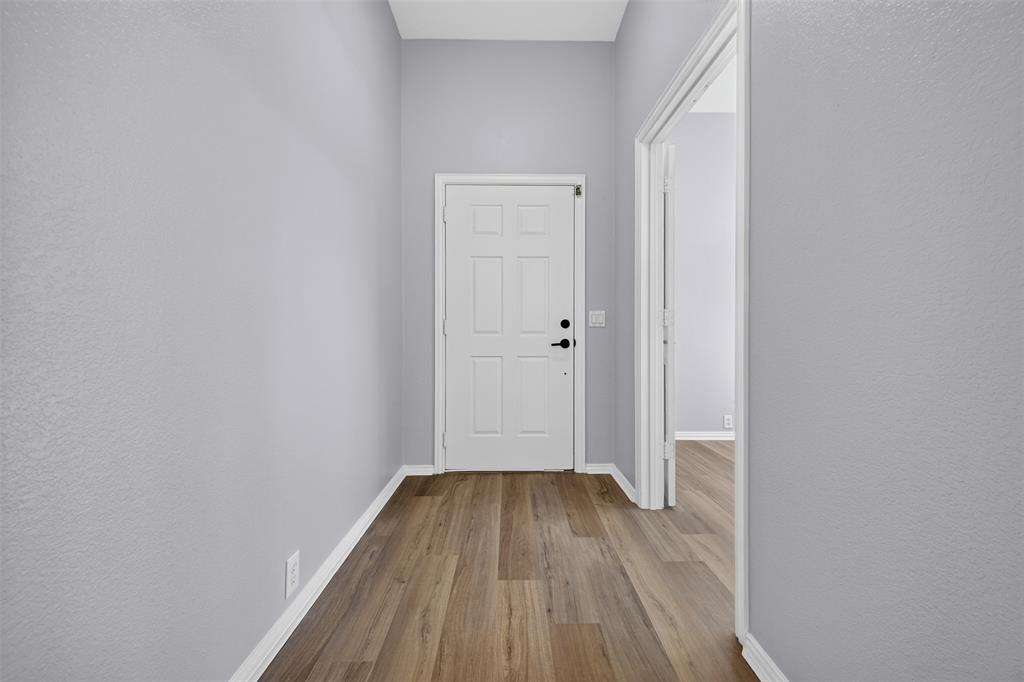 Entryway featuring a six-panel door with matte black hardware, neutral interior paint, and wood-finish flooring