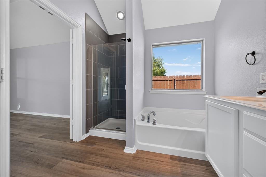 Bathroom featuring a glass-enclosed shower with tiled surround, a deep soaking tub, wood-finish flooring, and a vaulted ceiling