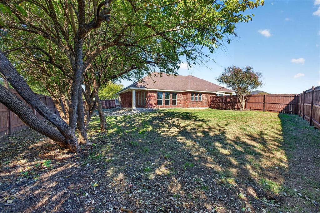 Backyard featuring a red brick exterior, mature trees, wood privacy fencing, and a covered patio