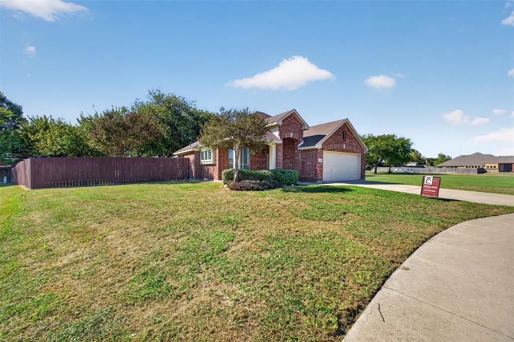 Single-story brick exterior featuring a multi-gable roofline, two-car garage, concrete driveway, and wooden perimeter fencing