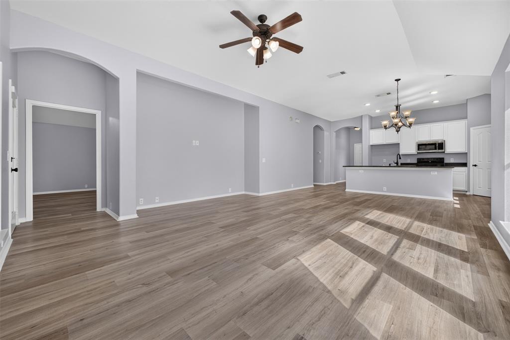 Open-concept living space featuring wood-finish flooring, high ceilings with recessed lighting, an architectural arched entry, a ceiling fan with integrated lighting, and a multi-tiered chandelier