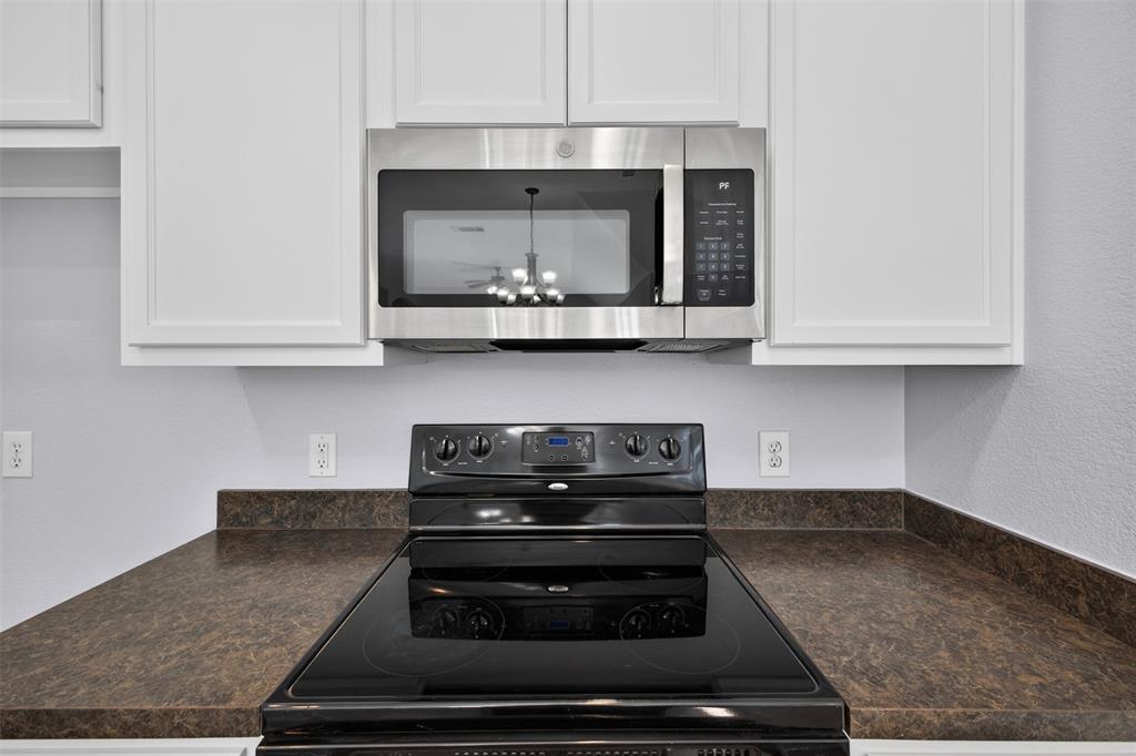Kitchen featuring white cabinetry, dark countertops, and stainless steel microwave paired with a black glass-top range