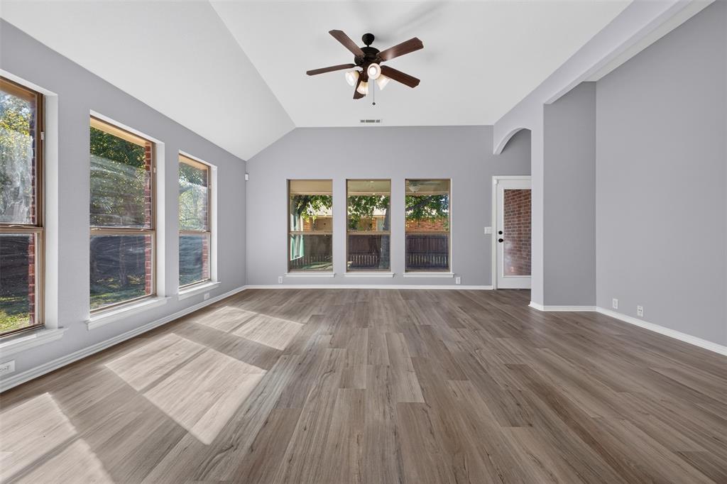 Vaulted ceiling featuring a central multi-blade ceiling fan, wood-finish flooring, and expansive windows