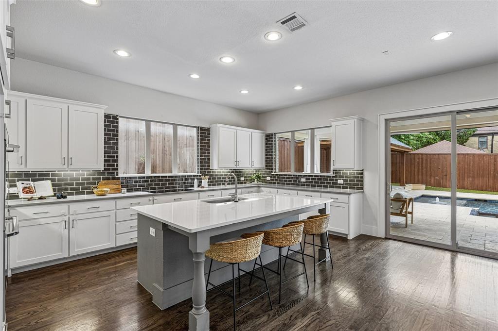 Kitchen featuring white cabinetry, a center island with a contrasting base and light-toned countertop, dark subway tile backsplash, wood-finish flooring, and recessed lighting