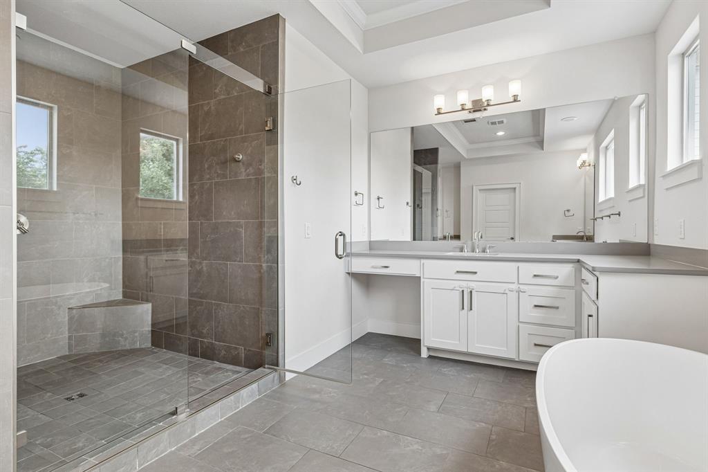 Walk-in shower with stone tile surround, integrated bench, glass enclosure, freestanding soaking tub, and white dual-sink vanity with stone countertop