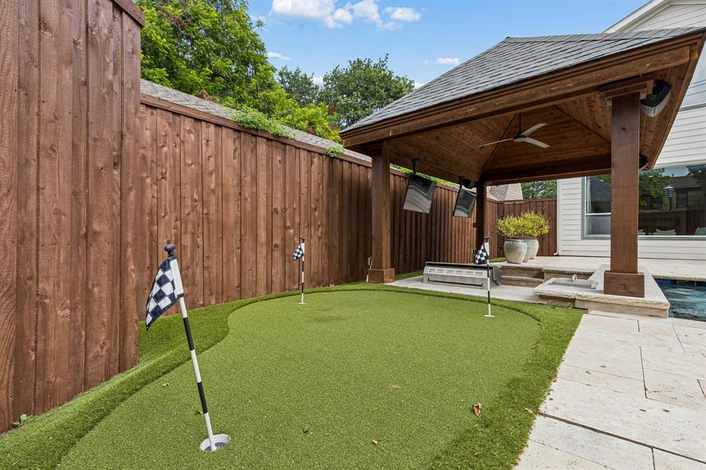 Backyard putting green featuring synthetic turf, surrounded by a wood privacy fence and a stone paver patio