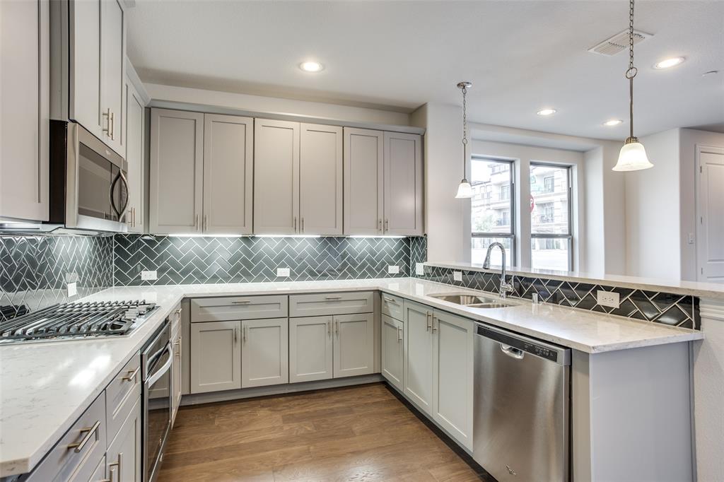 Kitchen featuring light-toned cabinetry, herringbone-patterned tile backsplash, stone-finish countertops, stainless steel appliances, and wood-finish flooring