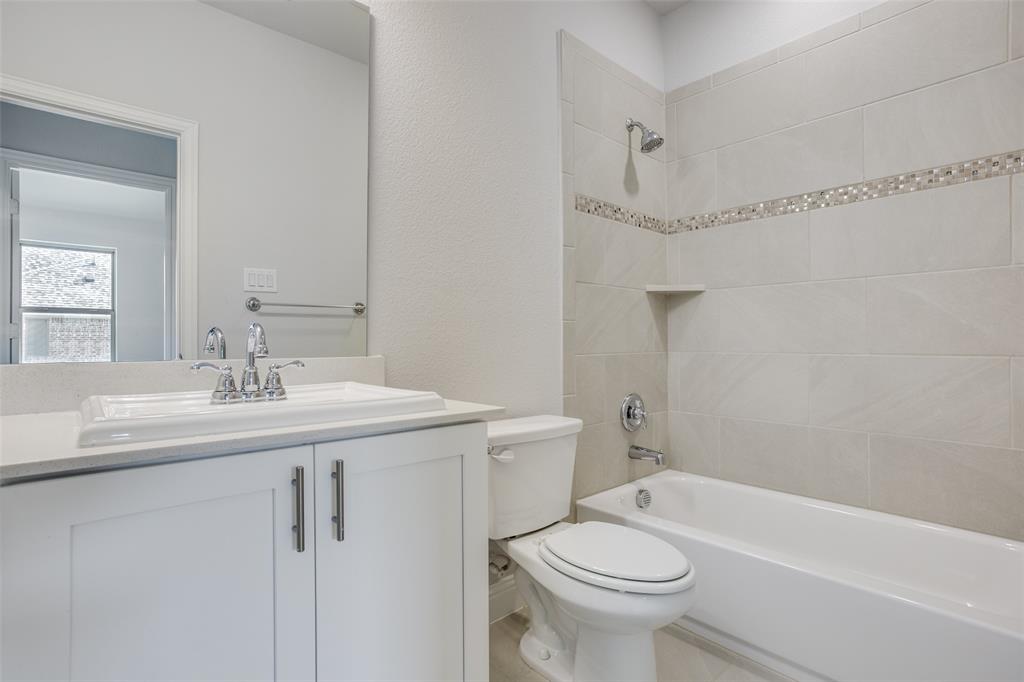 White vanity with a rectangular sink, polished chrome widespread faucet, large wall-mounted mirror, and a tub-shower combination featuring horizontal tile surrounds with a decorative mosaic inlay
