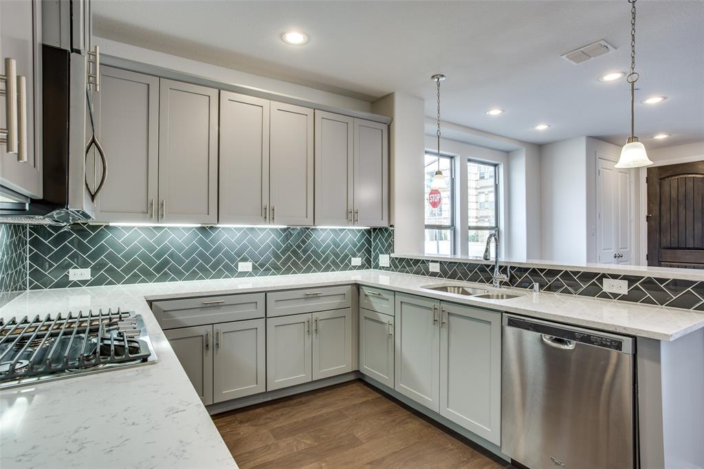 Kitchen featuring shaker-style cabinetry, quartz countertops, herringbone-pattern tile backsplash, stainless steel appliances, and wood-finish flooring