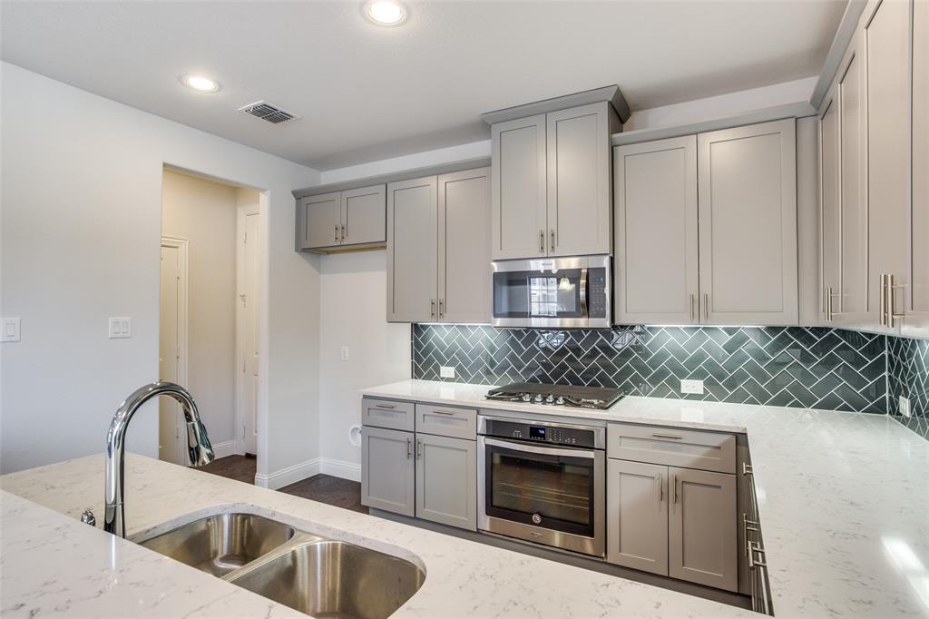 Kitchen featuring grey shaker-style cabinetry, white countertops with grey veining, a herringbone-patterned tile backsplash, stainless steel appliances, and a double-basin undermount sink with a pull-down faucet