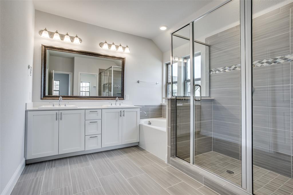 Dual-sink vanity with white cabinetry and countertop, framed wall mirror, deep soaking tub, and glass-enclosed shower with horizontal wall tile
