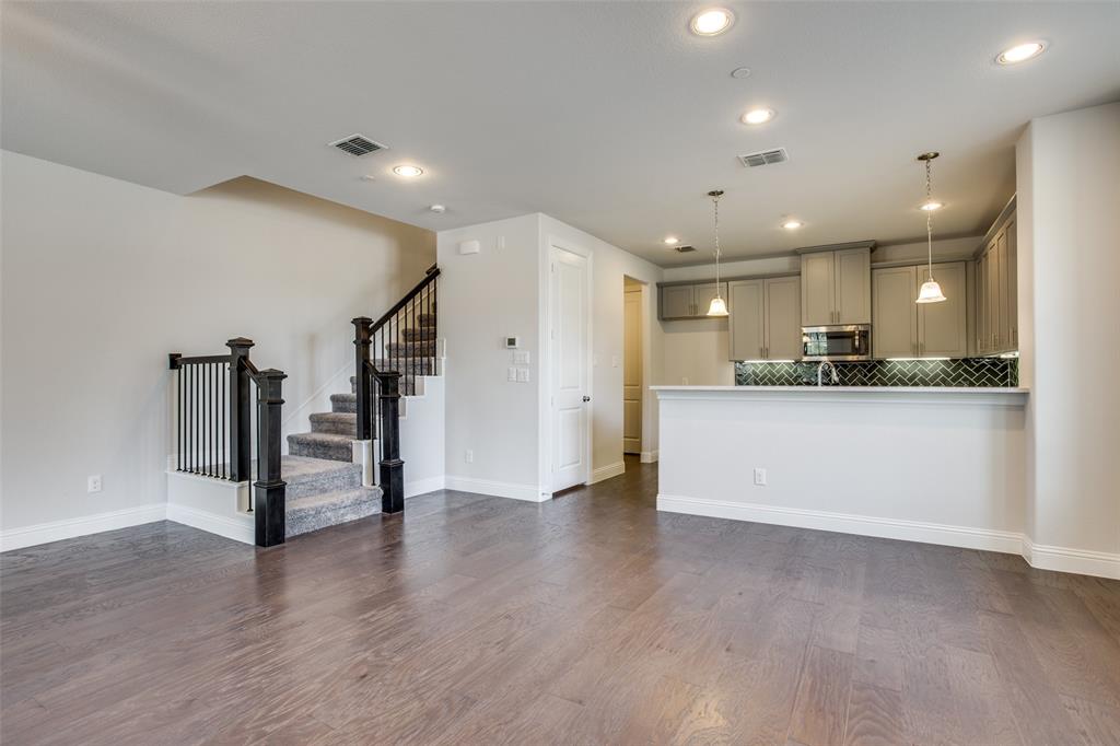 Open-concept interior featuring wood-finish flooring, recessed lighting, a kitchen breakfast bar, herringbone-patterned tile backsplash, and a staircase with stained-wood handrails Open-concept interior featuring wood-finish flooring, recessed lighting, a kitchen breakfast bar, herringbone-patterned tile backsplash, and a staircase with stained-wood handrails