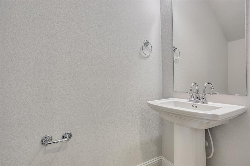 Pedestal sink with a polished chrome faucet, wall-mounted mirror, and matching chrome hardware fixtures